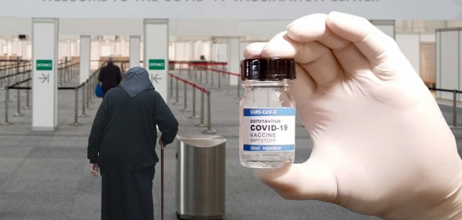 Eine ältere Frau auf dem Weg zu einem Impfzentrum. Im Vordergrund hält eine Hand in einem Handschuh eine Impfdose für Covid-19