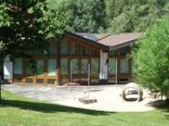 Außengelände der Kita Niederwetz. Im Vordergrund sieht man die grüne Spielwiese mit dem großen Sandkasten und im Hintergrund das Gebäude