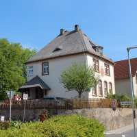 Die alte Schule in Laufdorf. Von weiter weg fotografiert. Um die alte Schule herum, blühen grüne Bäume und die Sonne bescheint diese