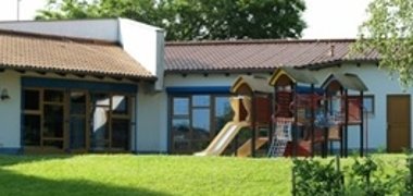 Das Außengelände der Kindertagesstätte in Schwalbach. Im Vordergrund sieht man das Spielgerüst auf einer großen grünen Wiese und im Hintergrund das Gebäude
